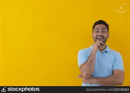 Portrait of a cheerful young man looking elsewhere with hand on chin against yellow background