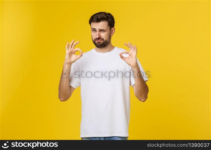 Portrait of a cheerful young man showing okay gesture isolated on yellow background.. Portrait of a cheerful young man showing okay gesture isolated on yellow background