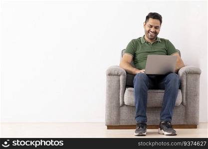 Portrait of a cheerful young man using laptop while sitting on sofa 