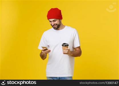 Portrait of a cheerful young man wearing casual clothes standing isolated over yellow background, holding mobile phone, drinking takeaway coffee. Portrait of a cheerful young man wearing casual clothes standing isolated over yellow background, holding mobile phone, drinking takeaway coffee.