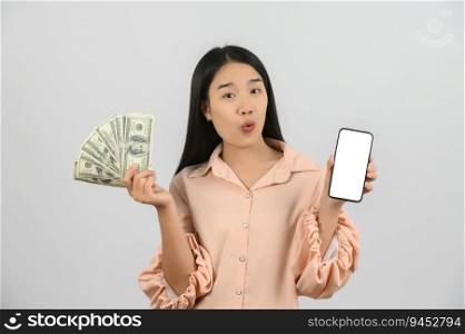 Portrait of a cheerful young woman holding money banknotes and showing smartphone mockup isolated over white background. Finance, currency, payment and people concept.