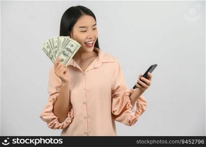 Portrait of a cheerful young woman holding money banknotes and using smartphone isolated over white background. Finance, currency, payment and people concept.
