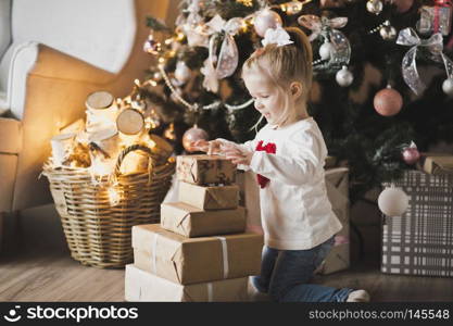 Portrait of a child sitting on the floor near the Christmas tree.. A little girl sitting under the Christmas tree with gifts 7249.