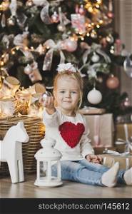 Portrait of a child sitting on the floor near the Christmas tree.. A little girl sitting under the Christmas tree with gifts 7240.