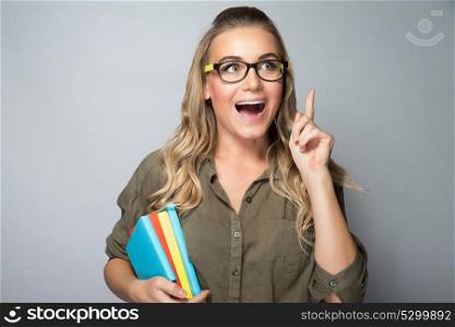 Portrait of a clever student girl, brilliant idea concept, excited woman standing with open mouth and finger up, shot over gray background, enjoying education in high school