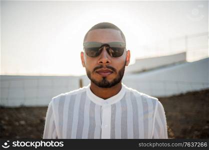 Portrait of a confident and casual man, modern muslim wearing sunglasses, natural outdoor light.