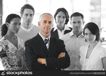 Portrait of a confident businessman standing arms crossed with office workers