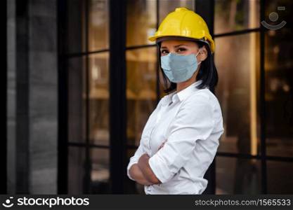 Portrait of a Confident Construction Engineer Woman. Wearing Surgical Protection Mask and Looking at Camera. Standing in front of the Modern Office Building