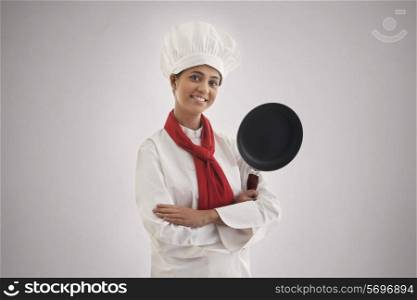 Portrait of a confident female chef holding frying pan isolated over gray background