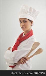Portrait of a confident female chef holding wooden spoon and spatula isolated over gray background