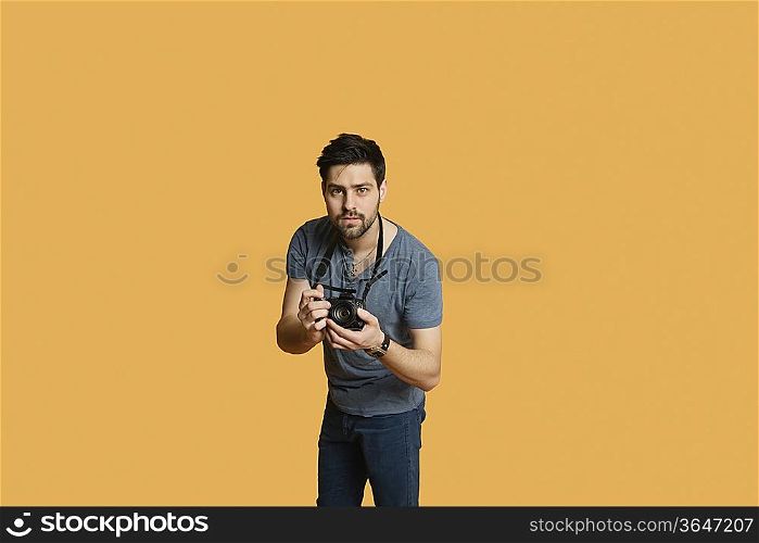 Portrait of a confident young man with camera over colored background