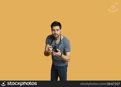 Portrait of a confident young man with camera over colored background