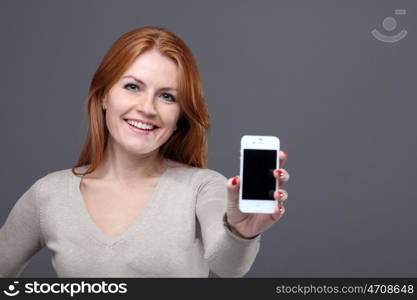 Portrait of a confident young woman showing mobile phone against grey background