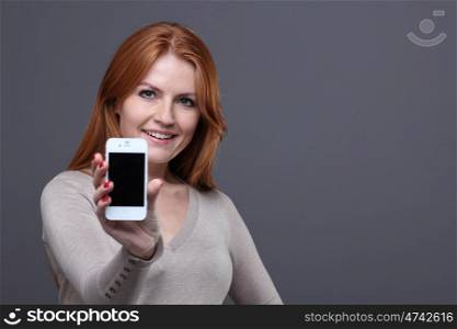 Portrait of a confident young woman showing mobile phone against grey background