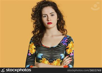 Portrait of a confident young woman with arms crossed over colored background