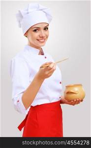 Portrait of a cook. Young female chef in red apron against grey background