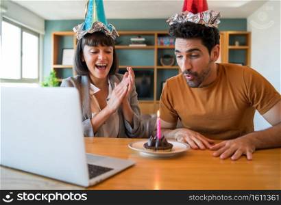 Portrait of a couple celebrating birthday on a video call with a laptop from home. Couple celebrating birthday online in quarantine time. New normal lifestyle concept.. Couple celebrating birthday on a video call at home.