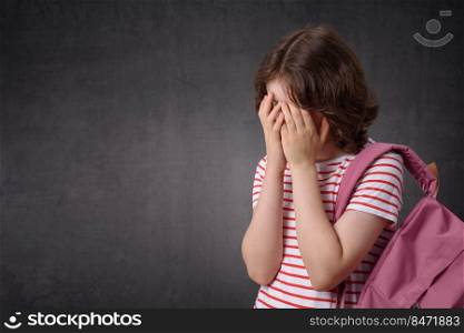 Portrait of a crying schoolgirl holding backpack, looking at camera. Crying schoolgirl holding backpack, looking at camera