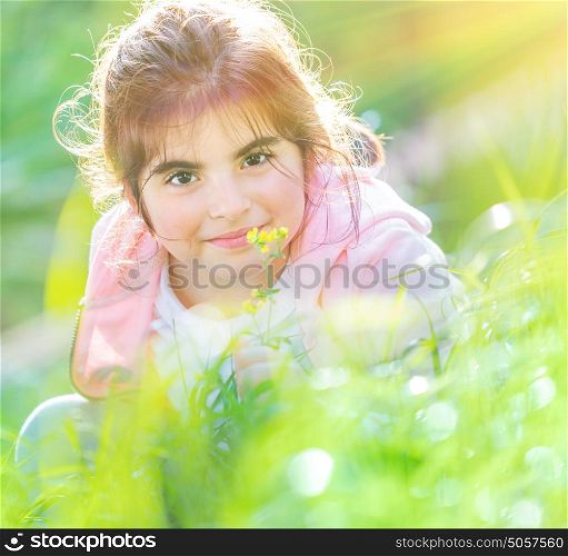 Portrait of a cute baby girl enjoying flowers aroma, having fun on fresh green grass field in spring sunny day, little child with pleasure spending time outdoors