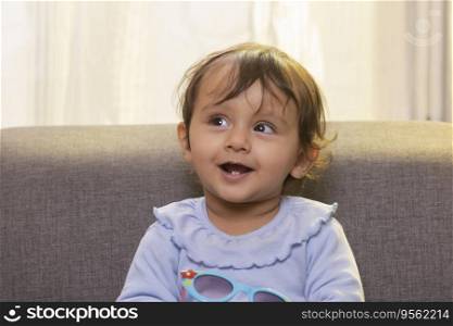 Portrait of a cute baby looking away with holding sunglass in living room