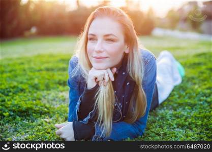Portrait of a cute blond female lying down on fresh green grass meadow on the backyard, enjoying warm sunny day, happy spring weekend in a countryside. Cute female on the spring meadow