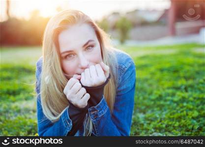 Portrait of a cute blond female lying down on fresh green grass meadow on the backyard, enjoying warm sunny day, happy spring weekend in a countryside. Cute girl on spring meadow