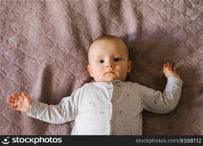 Portrait of a cute charming smiling white Caucasian boy of six months old lying on a bed and looking at the camera. View from above.