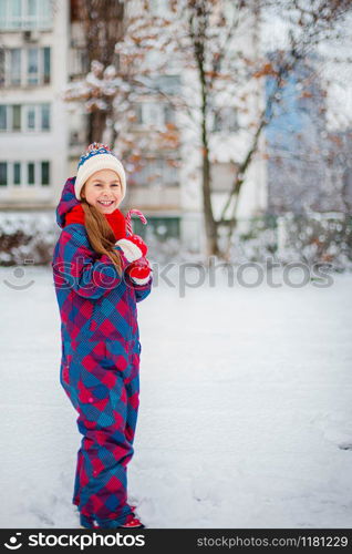 Portrait of a cute girl with christmas lollipop in hands on a winter street. Funny emotions on the face of the child.. Portrait of a cute girl with christmas lollipop in hands on a winter street.