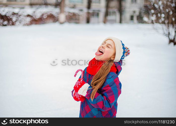 Portrait of a cute girl with christmas lollipop in hands on a winter street. Funny emotions on the face of the child.. Portrait of a cute girl with christmas lollipop in hands on a winter street.