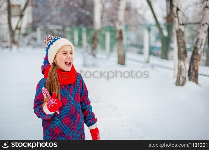 Portrait of a cute girl with christmas lollipop in hands on a winter street. Funny emotions on the face of the child.. Portrait of a cute girl with christmas lollipop in hands on a winter street.