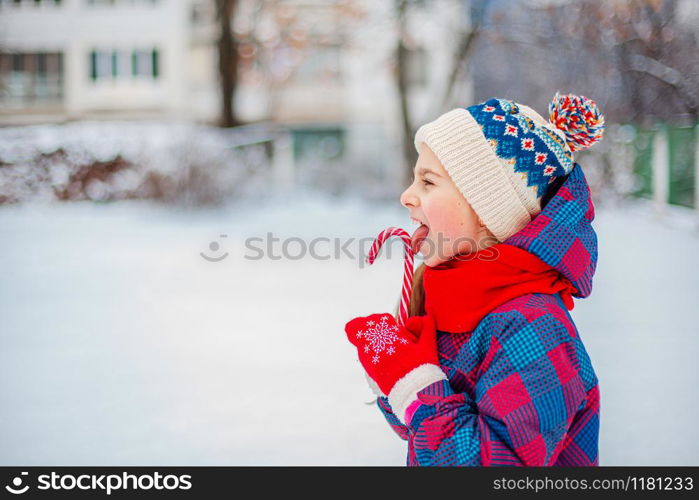 Portrait of a cute girl with christmas lollipop in hands on a winter street. Funny emotions on the face of the child.. Portrait of a cute girl with christmas lollipop in hands on a winter street.