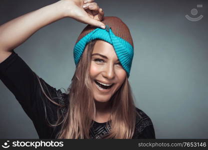 Portrait of a cute happy cheerful girl making faces and playing with a hat. Young model over gray background, funky urban style fashion for youngsters, joyful life