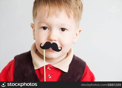 Portrait of a cute little boy with funny photo props paper mustache against a white background