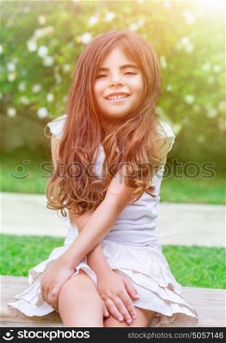 Portrait of a cute little girl sitting in the park and enjoying bright sunny day, having fun outdoors, spending time in daycare at summer camp, happy childhood concept