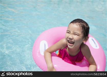 Portrait of a cute little girl swimming in the pool with a pink tube