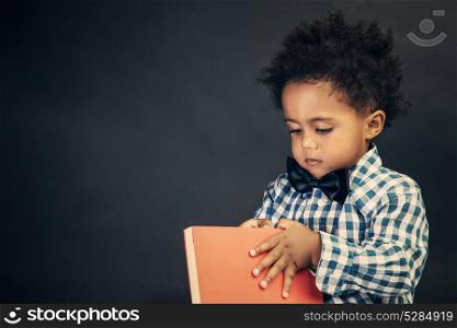 Portrait of a cute little schoolboy with book in hands over blackboard background, elementary school, back to school concept