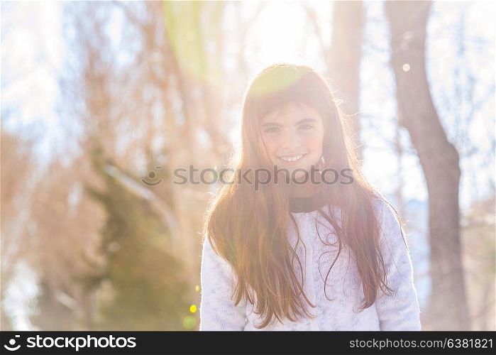 Portrait of a cute smiling little girl in the forest on bright sunny winter day, having fun outdoors, baby playing in a good warm weather the wintertime