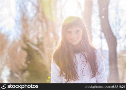 Portrait of a cute smiling little girl in the forest on bright sunny winter day, having fun outdoors, baby playing in a good warm weather the wintertime