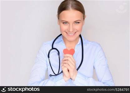 Portrait of a cute smiling woman cardiologist holding in hands little paper heart and wearing medical robe and stethoscope, happy doctor in the hospital, healthy life concept