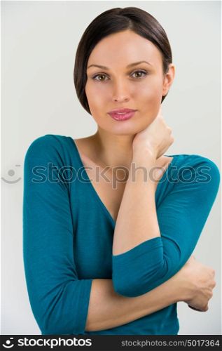 Portrait of a cute young woman standing with her hand folded against grey background