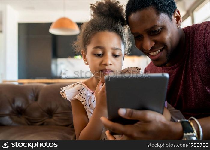 Portrait of a daughter and father having fun together and playing with digital tablet at home. Monoparental concept.