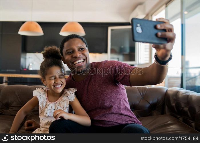 Portrait of a daughter and father having fun together and taking a selfie with mobile phone at home. Monoparental concept.