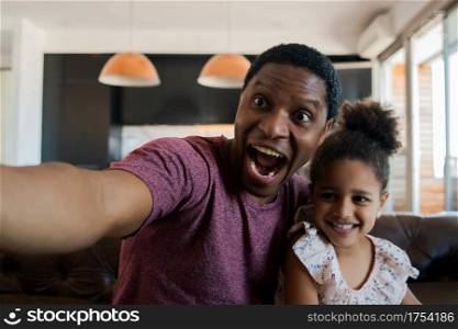 Portrait of a daughter and father having fun together and taking a selfie while sitting on couch at home. Monoparental concept.