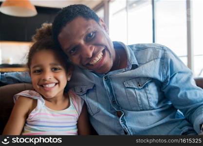 Portrait of a daughter and father smiling and sitting on couch at home. Monoparental concept.