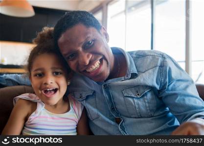 Portrait of a daughter and father smiling and sitting on couch at home. Monoparental concept.