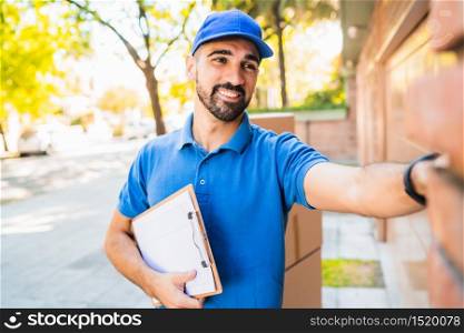 Portrait of a delivery man carrying packages while ringing house doorbell for making home delivery to his customer. Delivery and shipping concept.