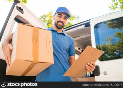 Portrait of a delivery man unloading cardboard boxes from van and checking clipboard list. Delivery service and shipping concept.