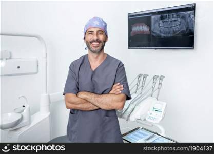 Portrait of a dentist in uniform and protective cap standing with arms crossed in a dental clinic. Portrait of a dentist standing with arms crossed in a clinic