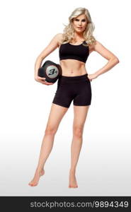 Portrait of a determined young white female athlete with curly long blond hair posing by herself holding a black medicine ball in a studio with white background wearing black shorts   sports bra.