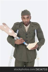 Portrait of a disabled military officer holding prosthesis leg with crutches standing over gray background